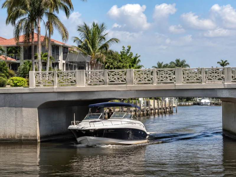 Boat passing under a Cape Coral canal bridge, showing the real overhead clearance that defines Gulf access